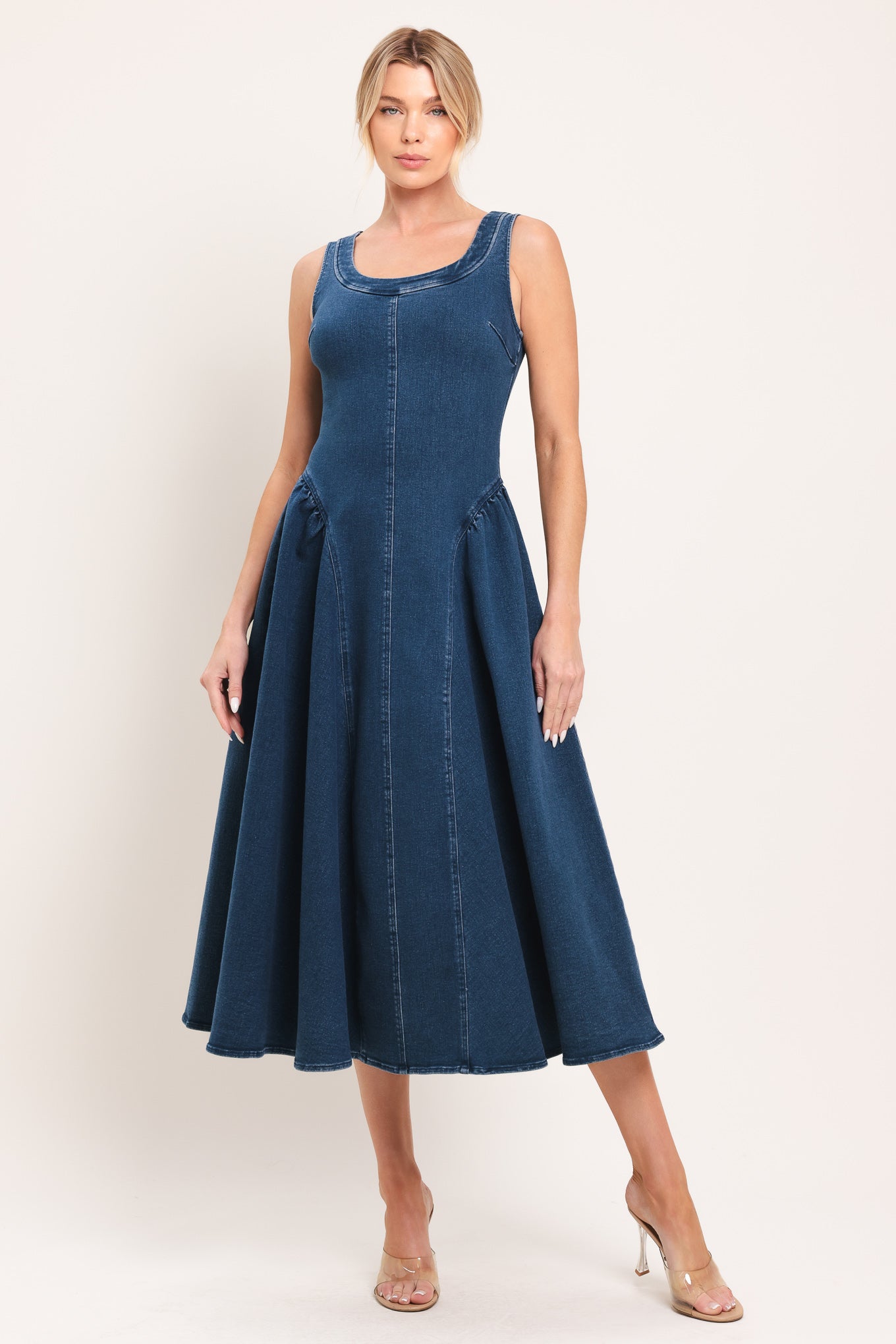 Woman wearing a sleeveless blue denim midi dress featuring U neckline, shirred side full skirt and back zipper closure | Flying Tomato