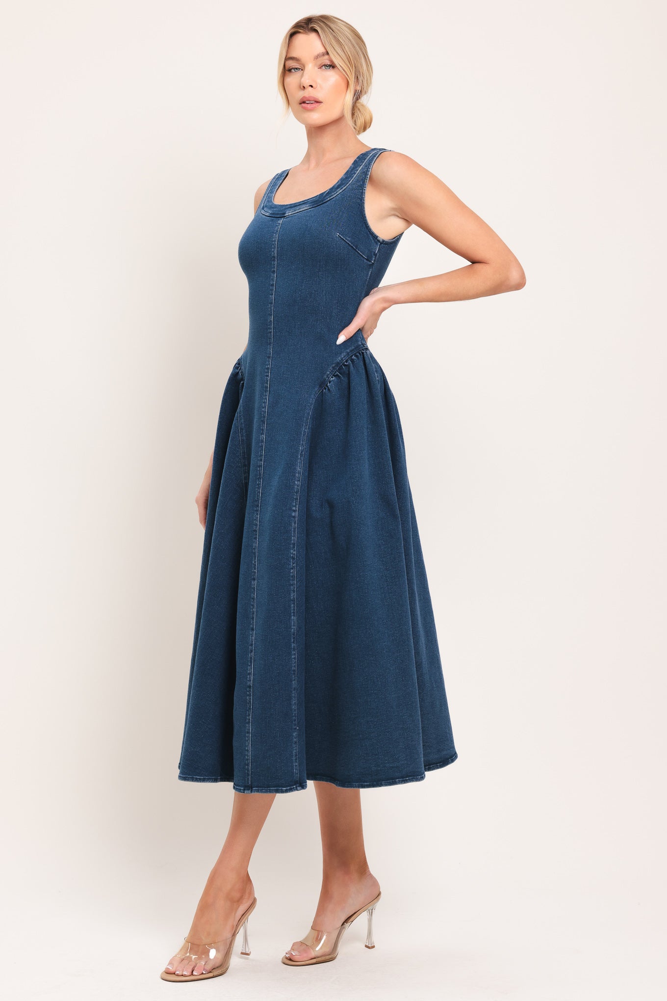 Woman wearing a sleeveless blue denim midi dress featuring U neckline, shirred side full skirt and back zipper closure | Flying Tomato