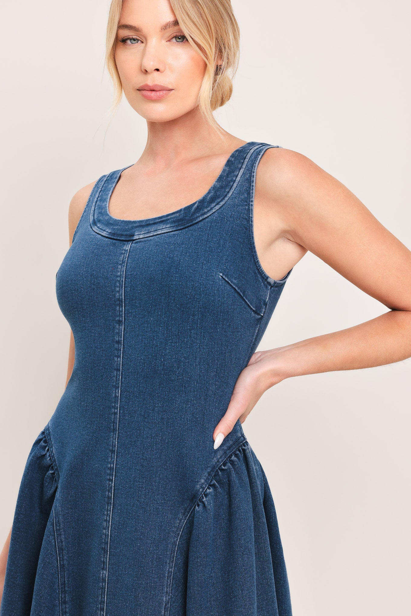 Woman wearing a sleeveless blue denim midi dress featuring U neckline, shirred side full skirt and back zipper closure | Flying Tomato