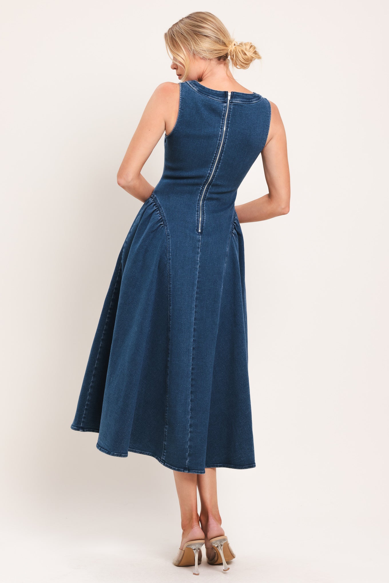Woman wearing a sleeveless blue denim midi dress featuring U neckline, shirred side full skirt and back zipper closure | Flying Tomato