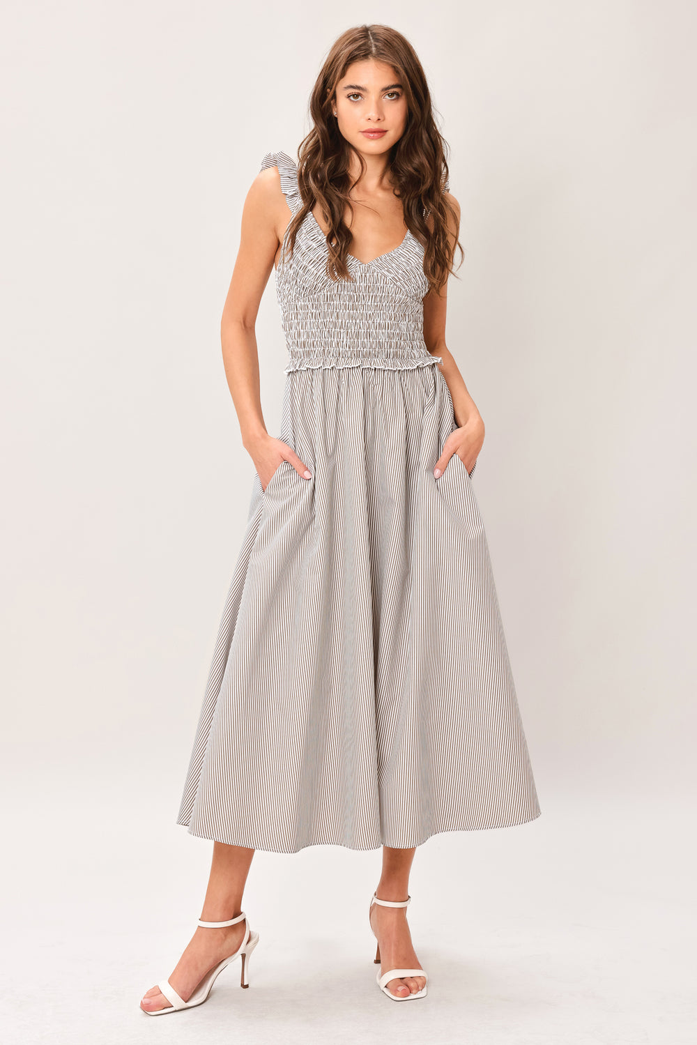 Woman wearing a taupe striped woven midi dress featuring smocked bodice, ruffle strap, side pockets and full skirt | Flying Tomato