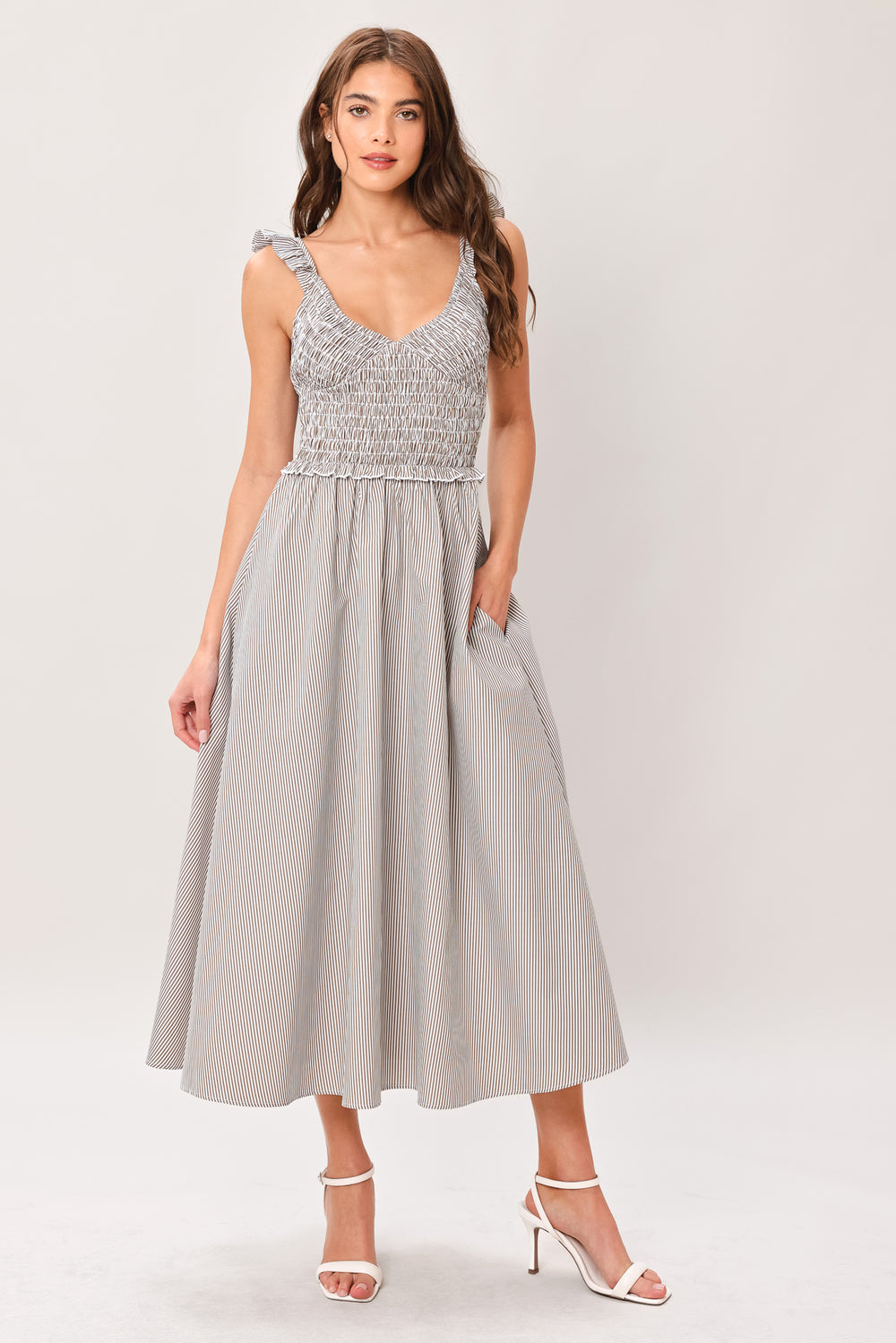 Woman wearing a taupe striped woven midi dress featuring smocked bodice, ruffle strap, side pockets and full skirt | Flying Tomato