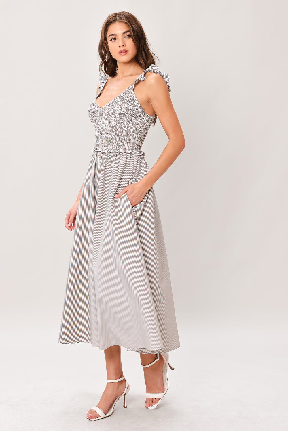 Woman wearing a taupe striped woven midi dress featuring smocked bodice, ruffle strap, side pockets and full skirt | Flying Tomato