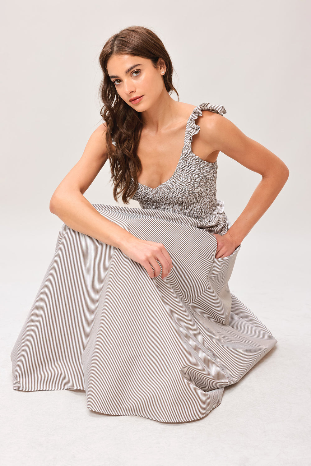 Woman wearing a taupe striped woven midi dress featuring smocked bodice, ruffle strap, side pockets and full skirt | Flying Tomato