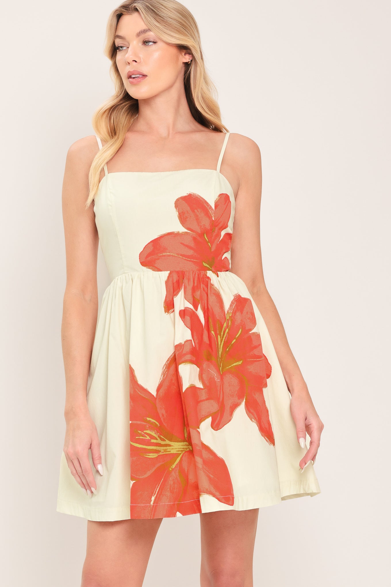 Woman wearing an off white with coral floral print mini dress with straps full skirt and back zipper closure | Flying Tomato
