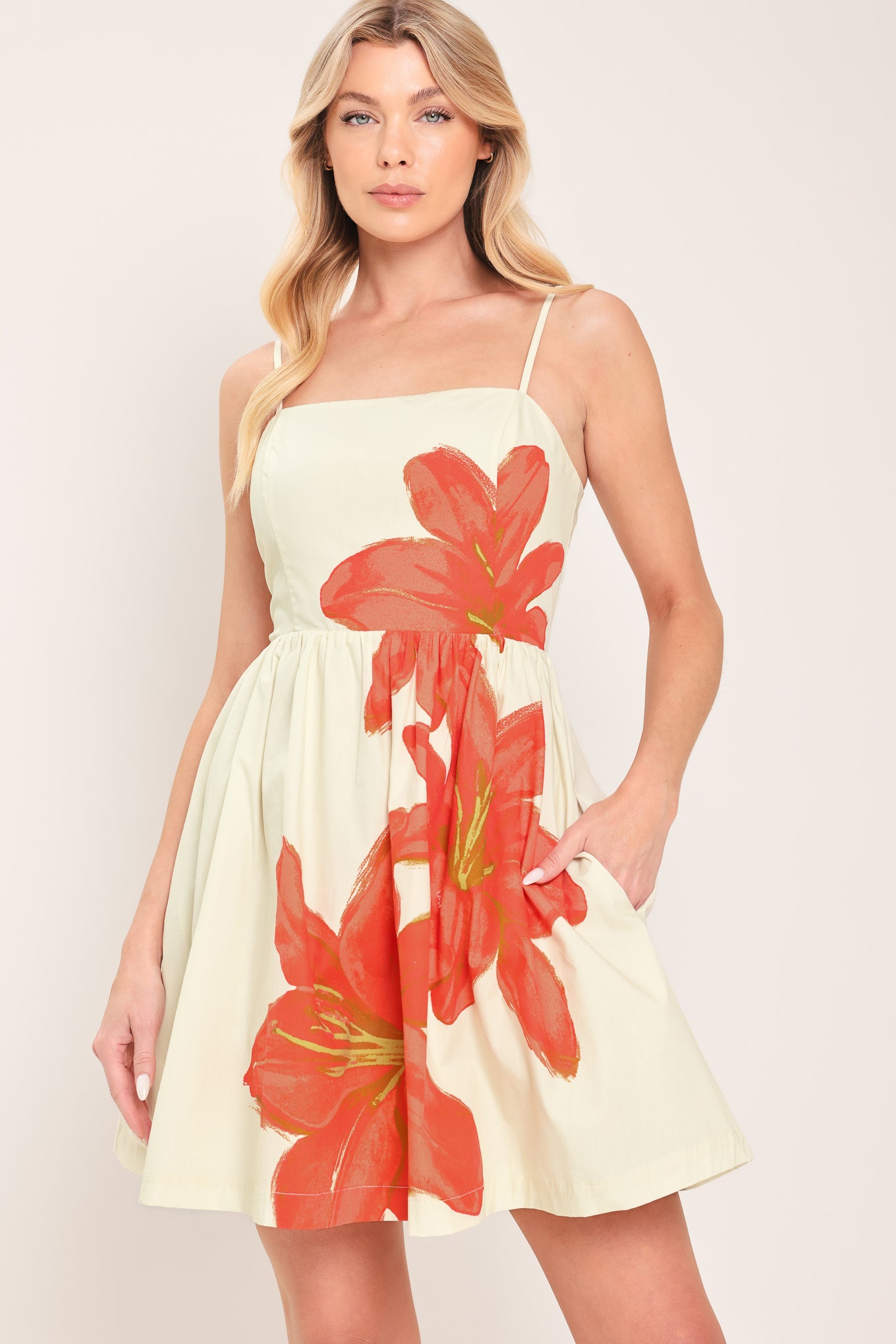 Woman wearing an off white with coral floral print mini dress with straps full skirt and back zipper closure | Flying Tomato