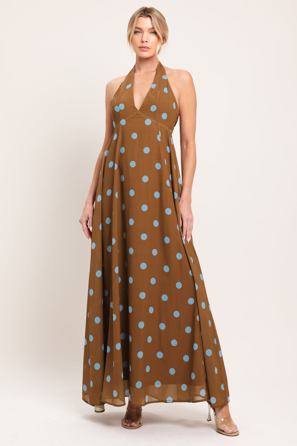 Woman wearing a brown with blue polka dots midi dress featuring halter neckline, circle skirt, bare back with tie neck and zipper closure | Flying Tomato