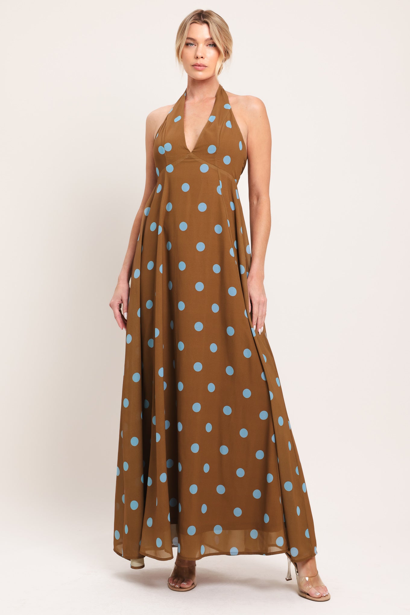 Woman wearing a brown with blue polka dots midi dress featuring halter neckline, circle skirt, bare back with tie neck and zipper closure | Flying Tomato