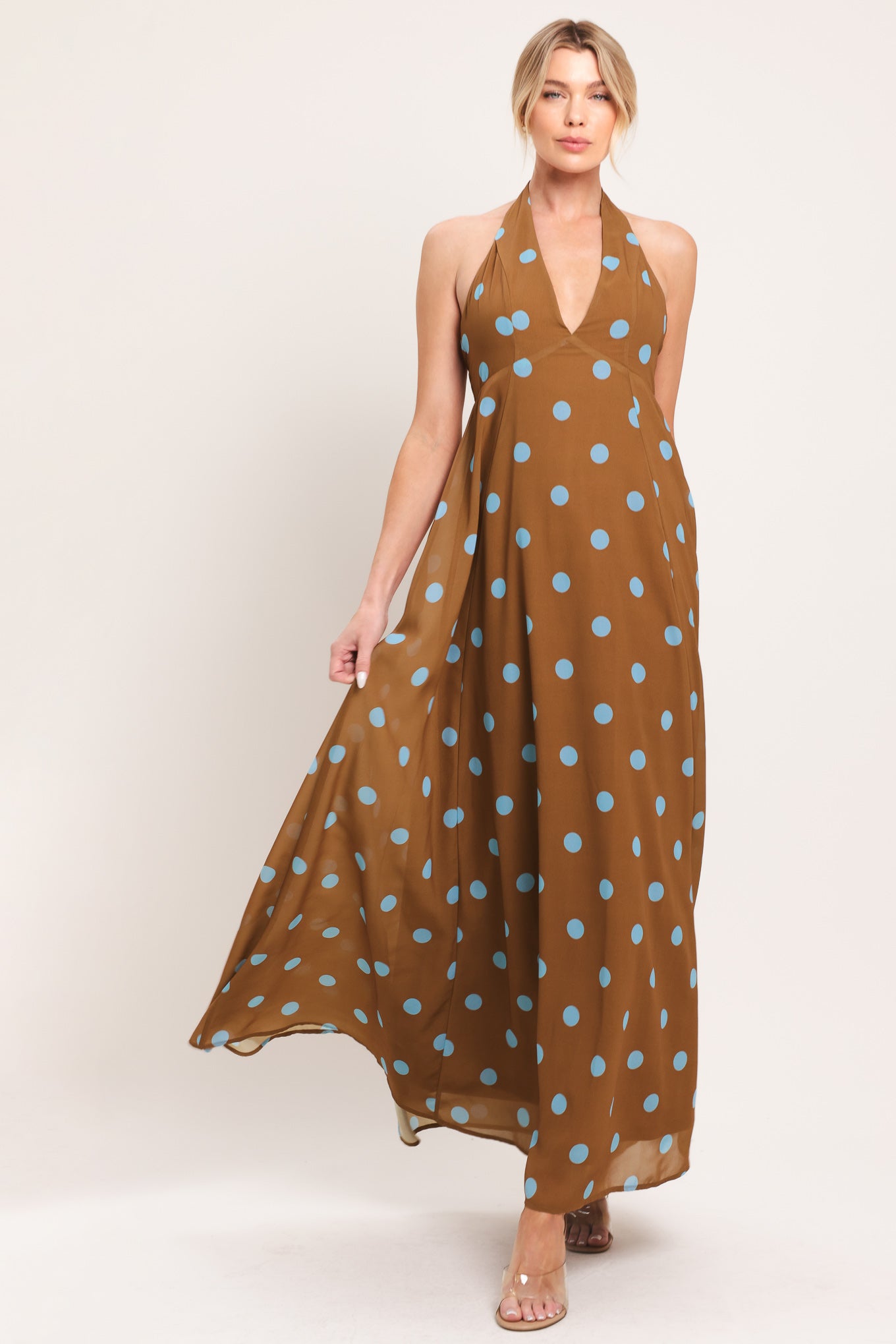 Woman wearing a brown with blue polka dots midi dress featuring halter neckline, circle skirt, bare back with tie neck and zipper closure | Flying Tomato