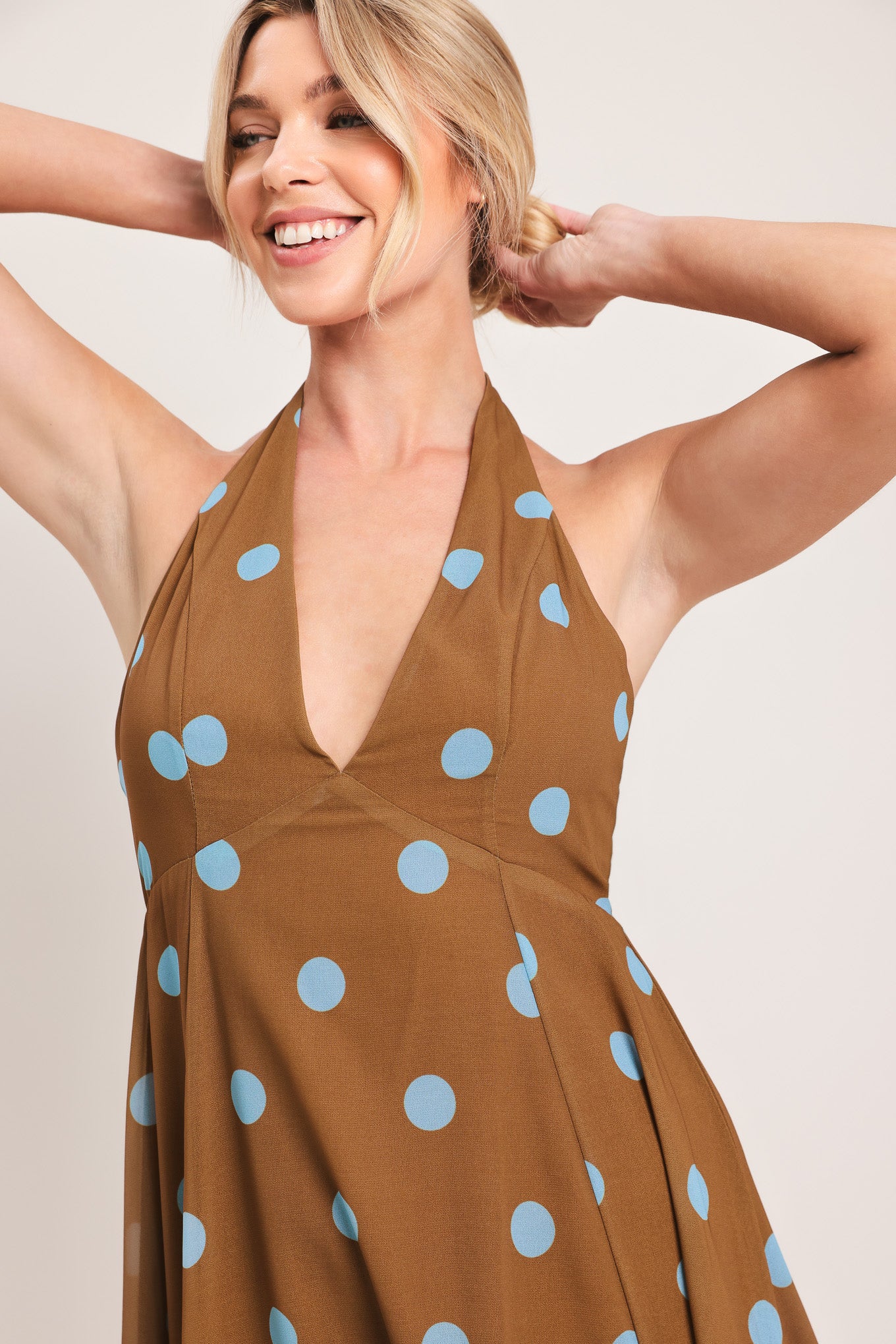 Woman wearing a brown with blue polka dots midi dress featuring halter neckline, circle skirt, bare back with tie neck and zipper closure | Flying Tomato