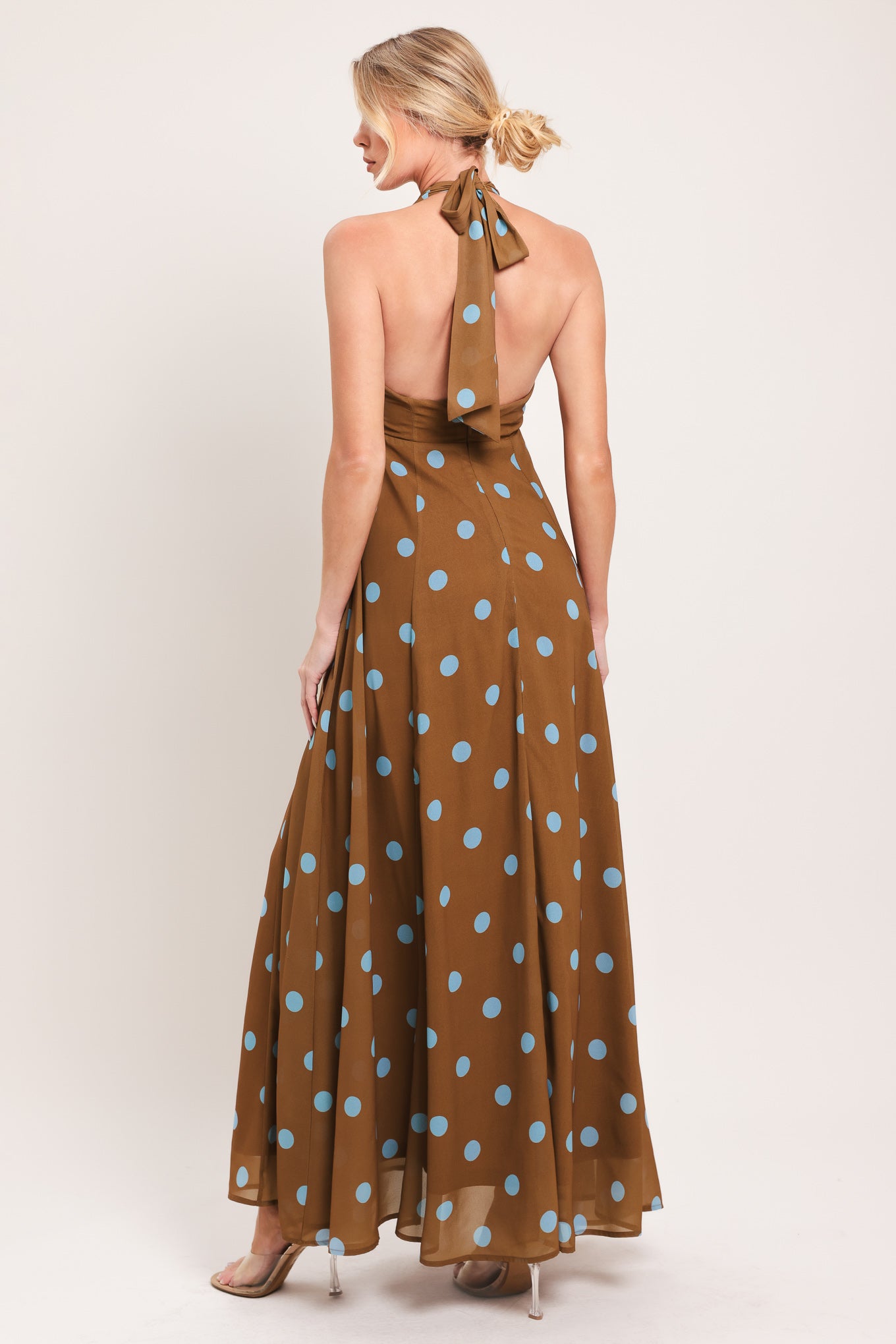 Woman wearing a brown with blue polka dots midi dress featuring halter neckline, circle skirt, bare back with tie neck and zipper closure | Flying Tomato