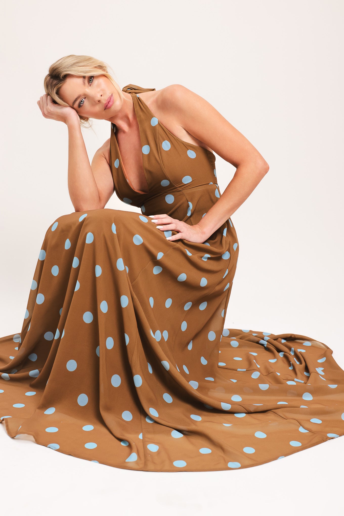 Woman wearing a brown with blue polka dots midi dress featuring halter neckline, circle skirt, bare back with tie neck and zipper closure | Flying Tomato