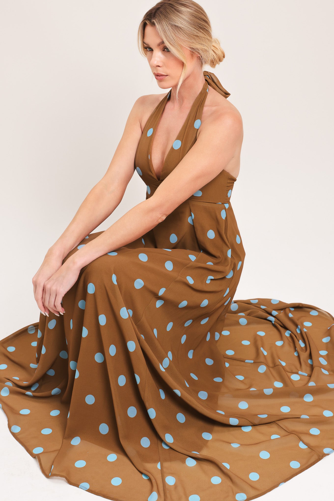 Woman wearing a brown with blue polka dots midi dress featuring halter neckline, circle skirt, bare back with tie neck and zipper closure | Flying Tomato