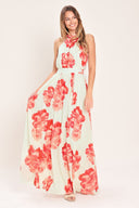 Woman wearing a cream colored with coral flowers maxi dress featuring halter neckline with back neck tie, full skirt and smocked back waistband | Flying Tomato