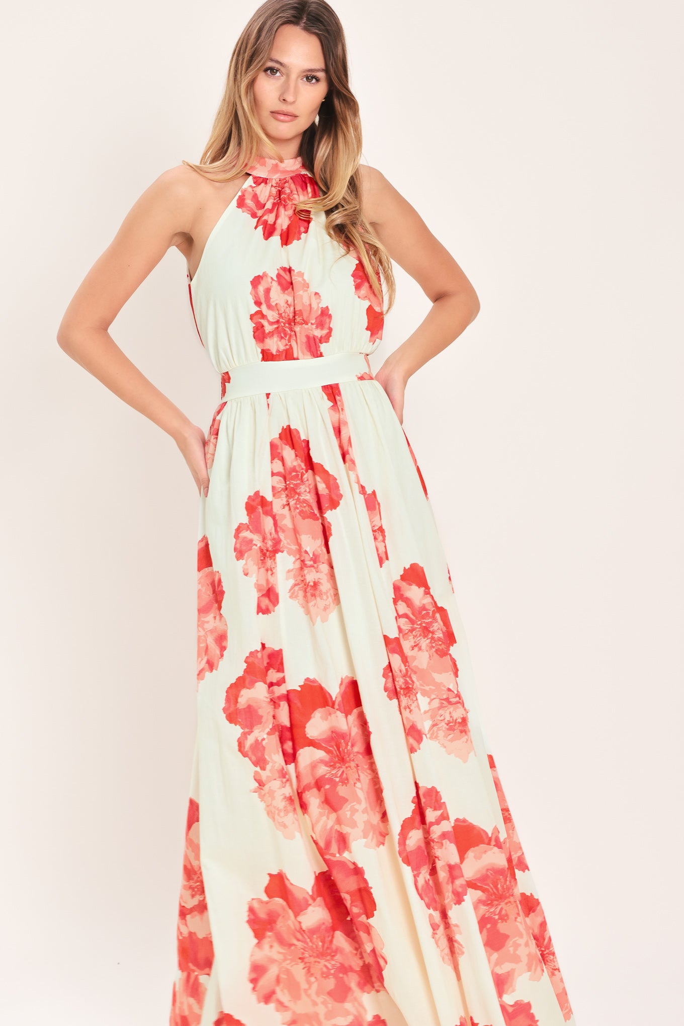 Woman wearing a cream colored with coral flowers maxi dress featuring halter neckline with back neck tie, full skirt and smocked back waistband | Flying Tomato