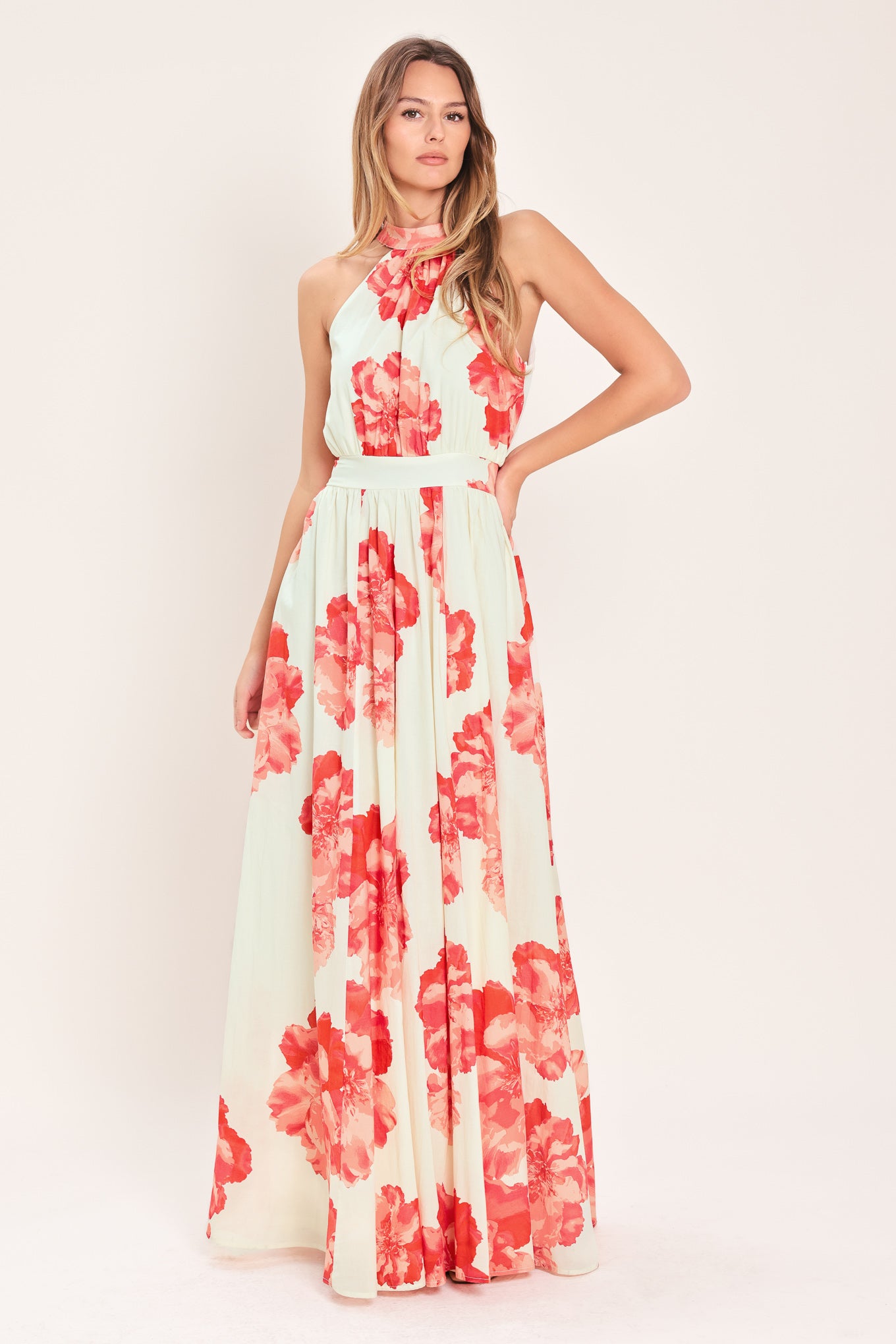 Woman wearing a cream colored with coral flowers maxi dress featuring halter neckline with back neck tie, full skirt and smocked back waistband | Flying Tomato