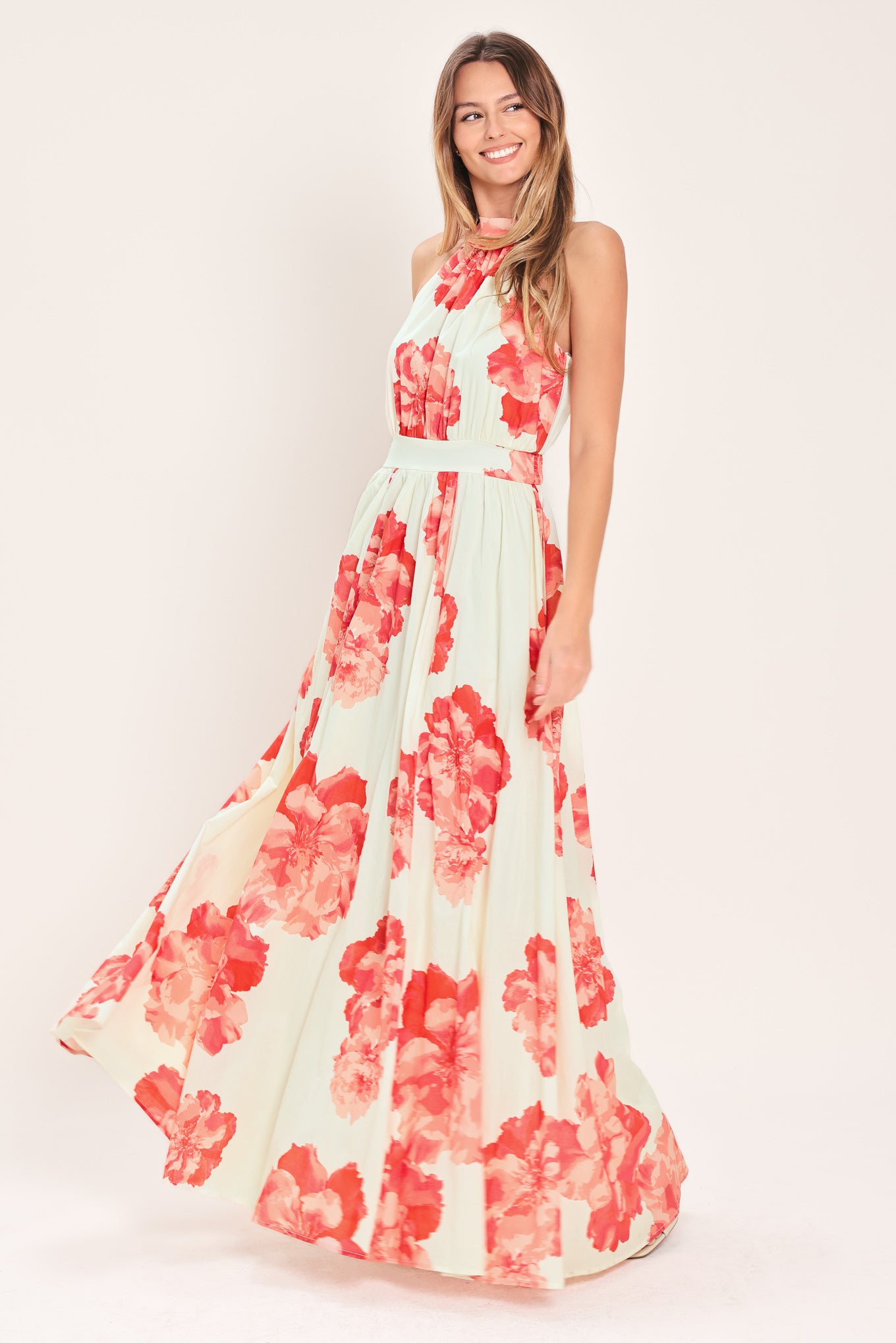 Woman wearing a cream colored with coral flowers maxi dress featuring halter neckline with back neck tie, full skirt and smocked back waistband | Flying Tomato