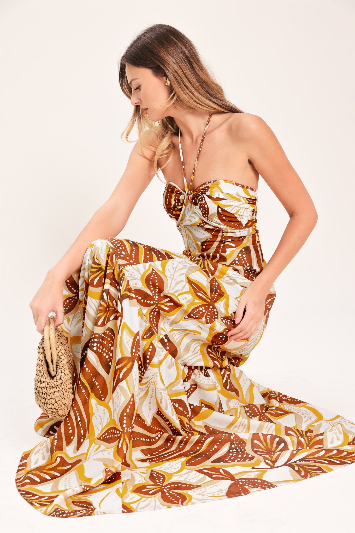 Woman wearing a mustard and brown tropical printed maxi dress featuring halter tie, ruffle hem and back zipper closure | Flying Tomato