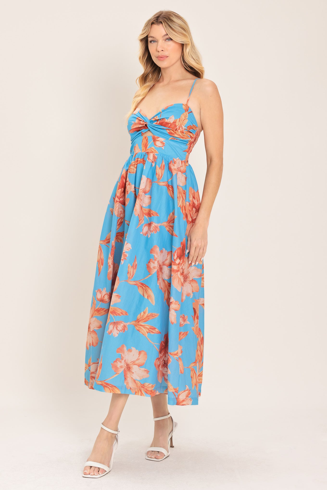 Woman wearing a blue with peach floral  pattern midi dress featuring twisted bodice with cut out, straps, full skirt and smocked back bodice | Flying Tomato