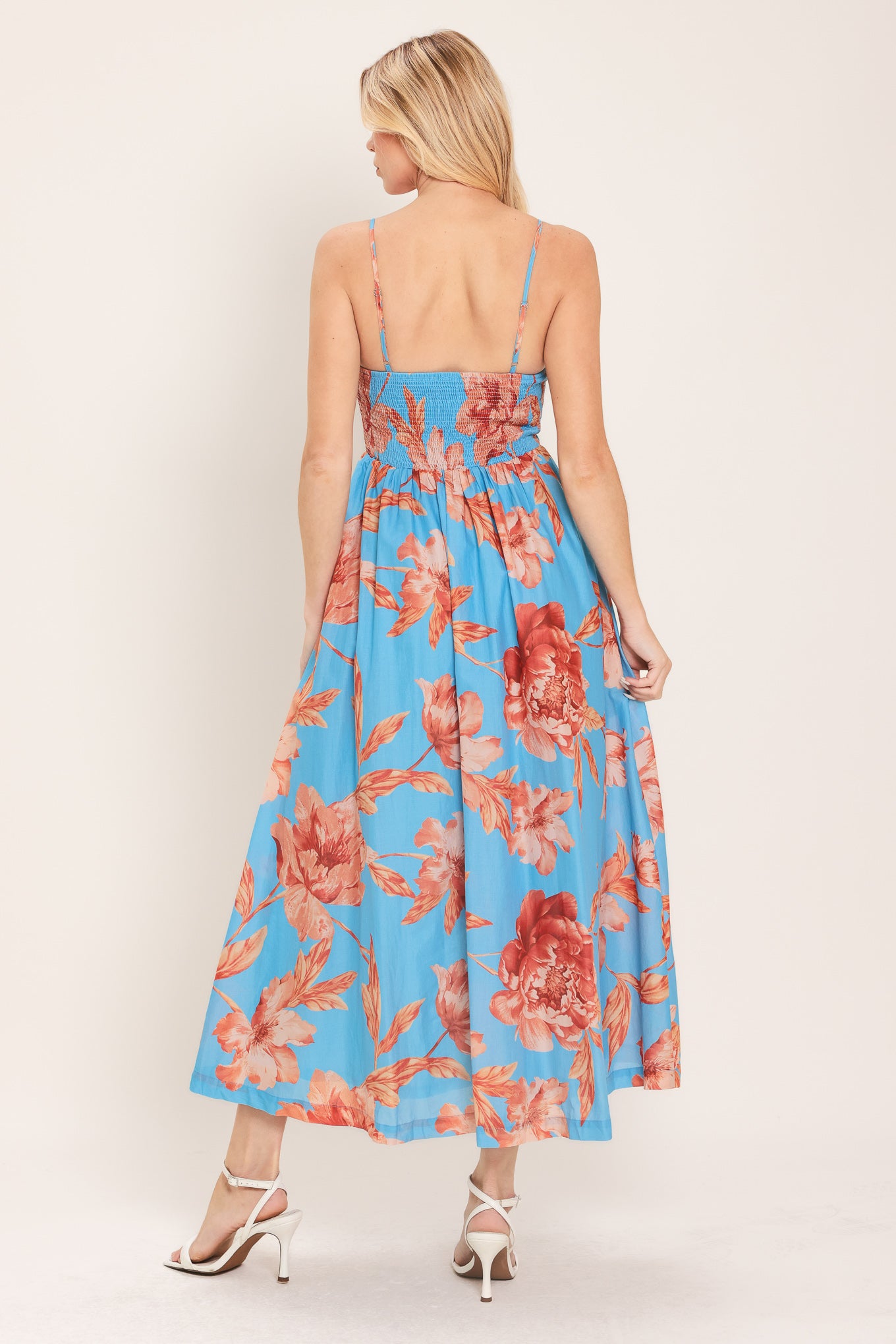 Woman wearing a blue with peach floral  pattern midi dress featuring twisted bodice with cut out, straps, full skirt and smocked back bodice | Flying Tomato