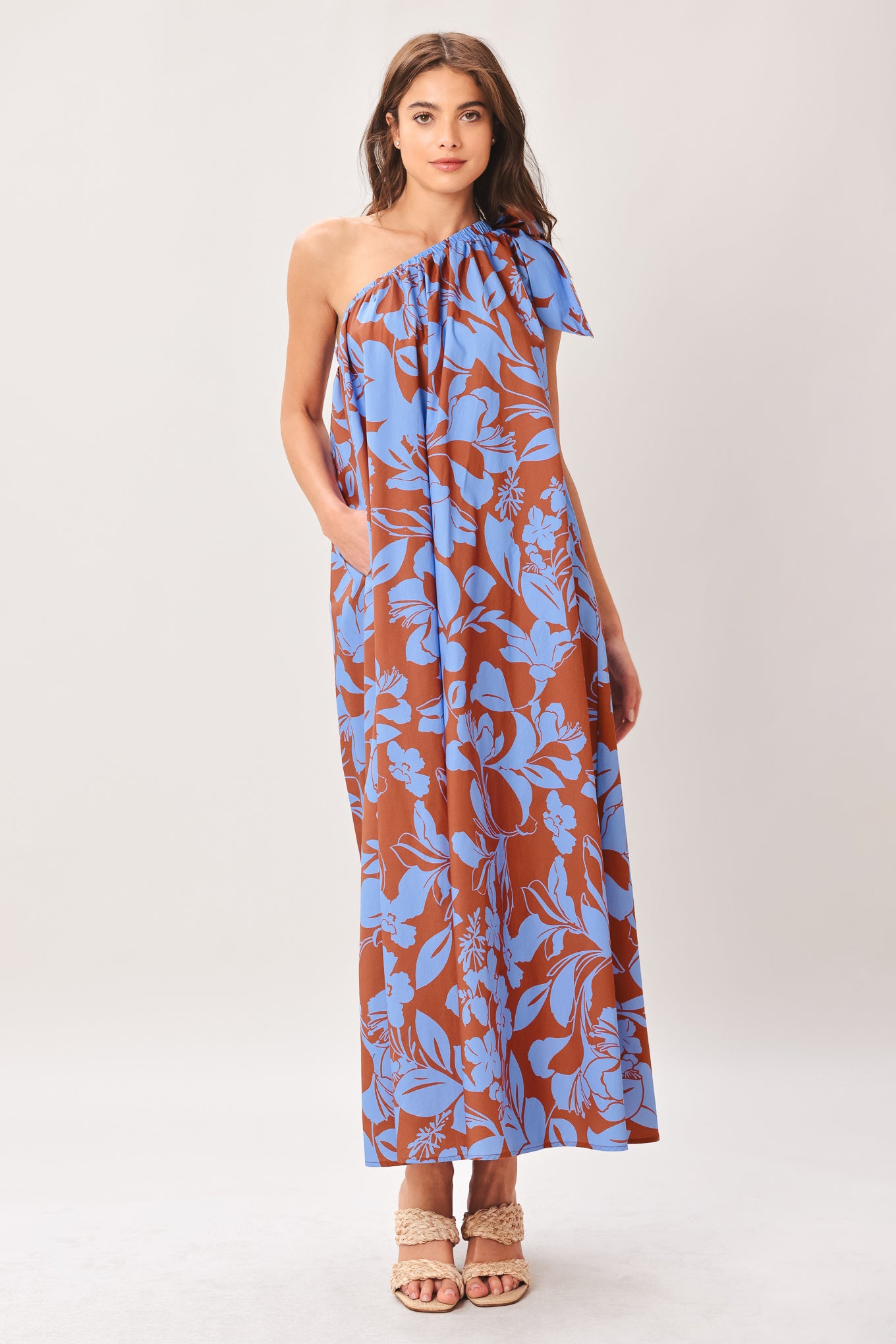 Woman wearing a blue and brown floral one-shoulder midi dress featuring bow tie shoulder and side pockets | Flying Tomato