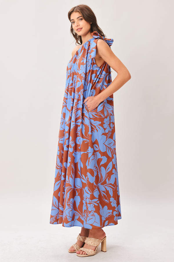 Woman wearing a blue and brown floral one-shoulder midi dress featuring bow tie shoulder and side pockets | Flying Tomato