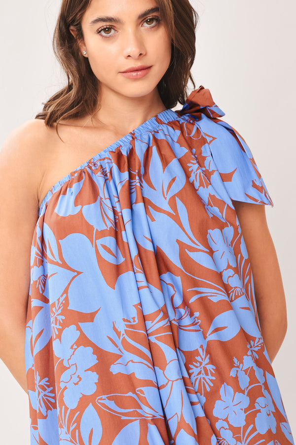 Woman wearing a blue and brown floral one-shoulder midi dress featuring bow tie shoulder and side pockets | Flying Tomato