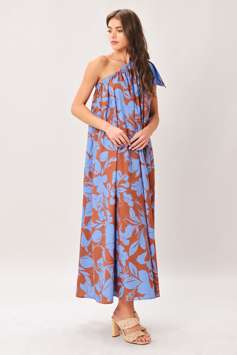 Woman wearing a blue and brown floral one-shoulder midi dress featuring bow tie shoulder and side pockets | Flying Tomato