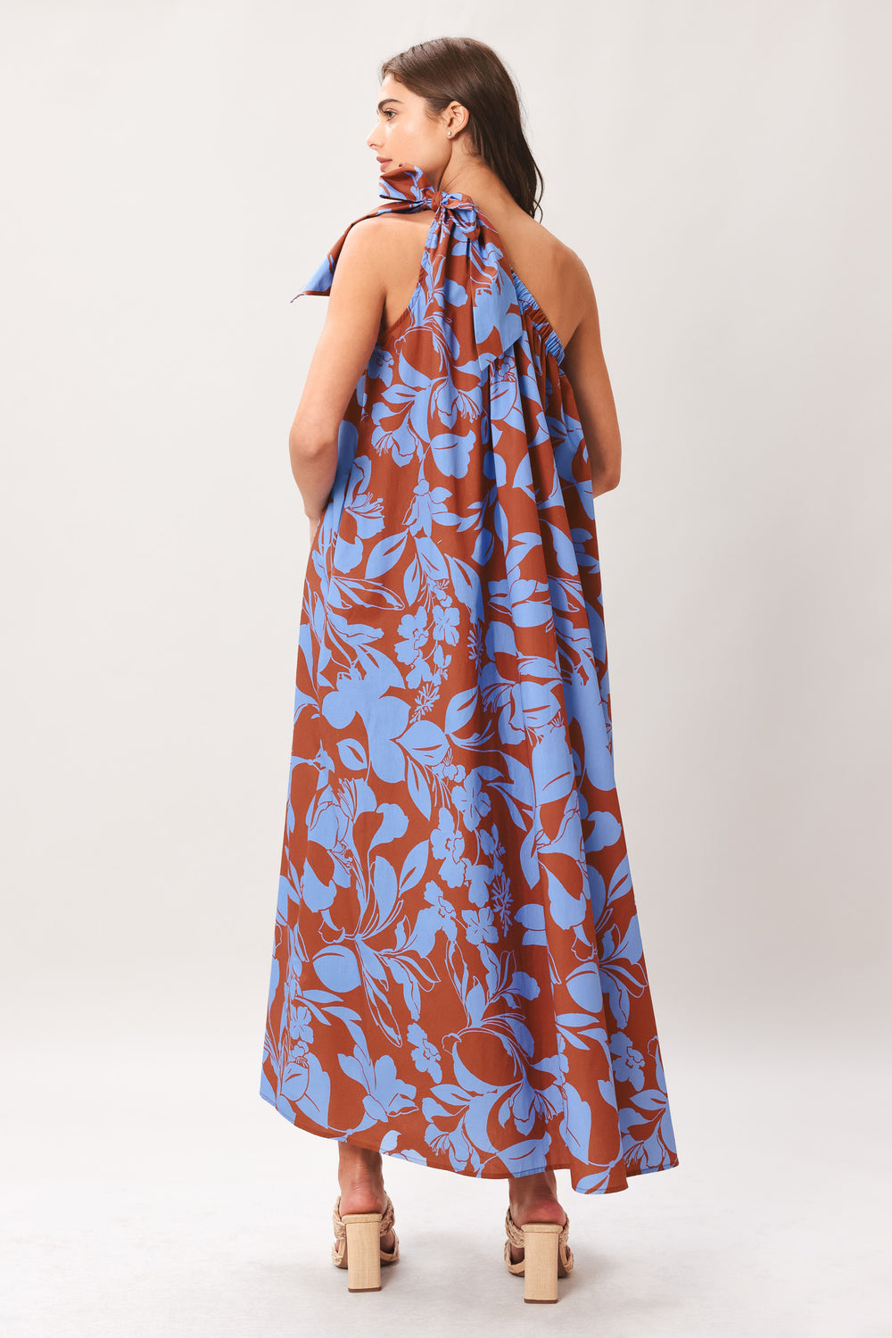 Woman wearing a blue and brown floral one-shoulder midi dress featuring bow tie shoulder and side pockets | Flying Tomato