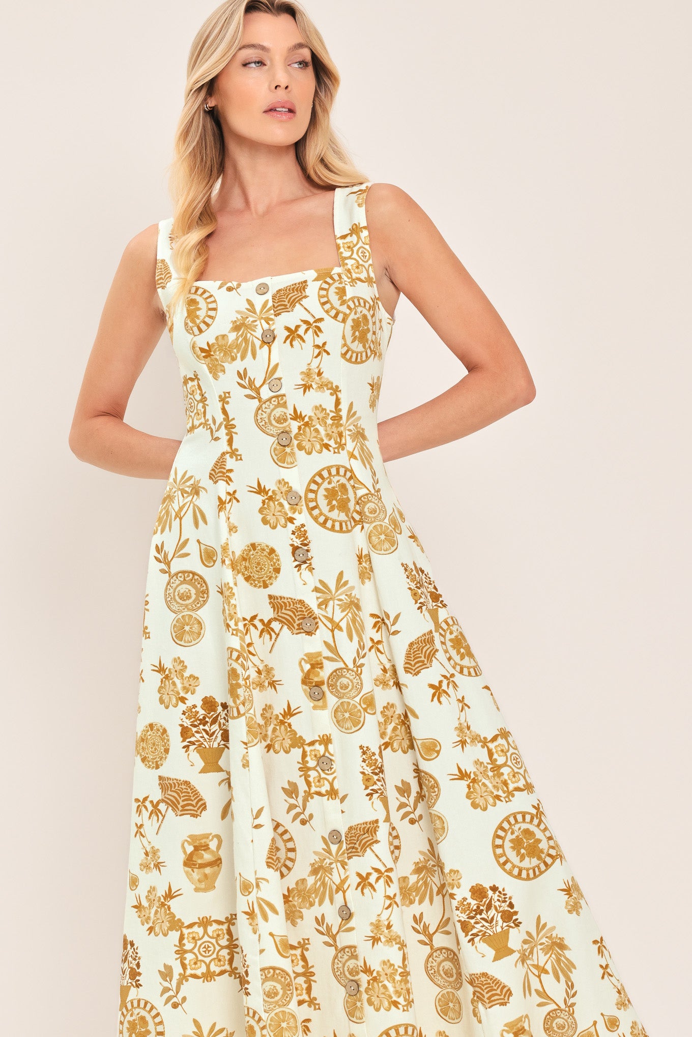 Woman wearing a yellow fruit and Mediterranean objects printed midi dress featuring square neckline, sleeveless, button down detail, circle skirt and back zipper closure | Flying Tomato