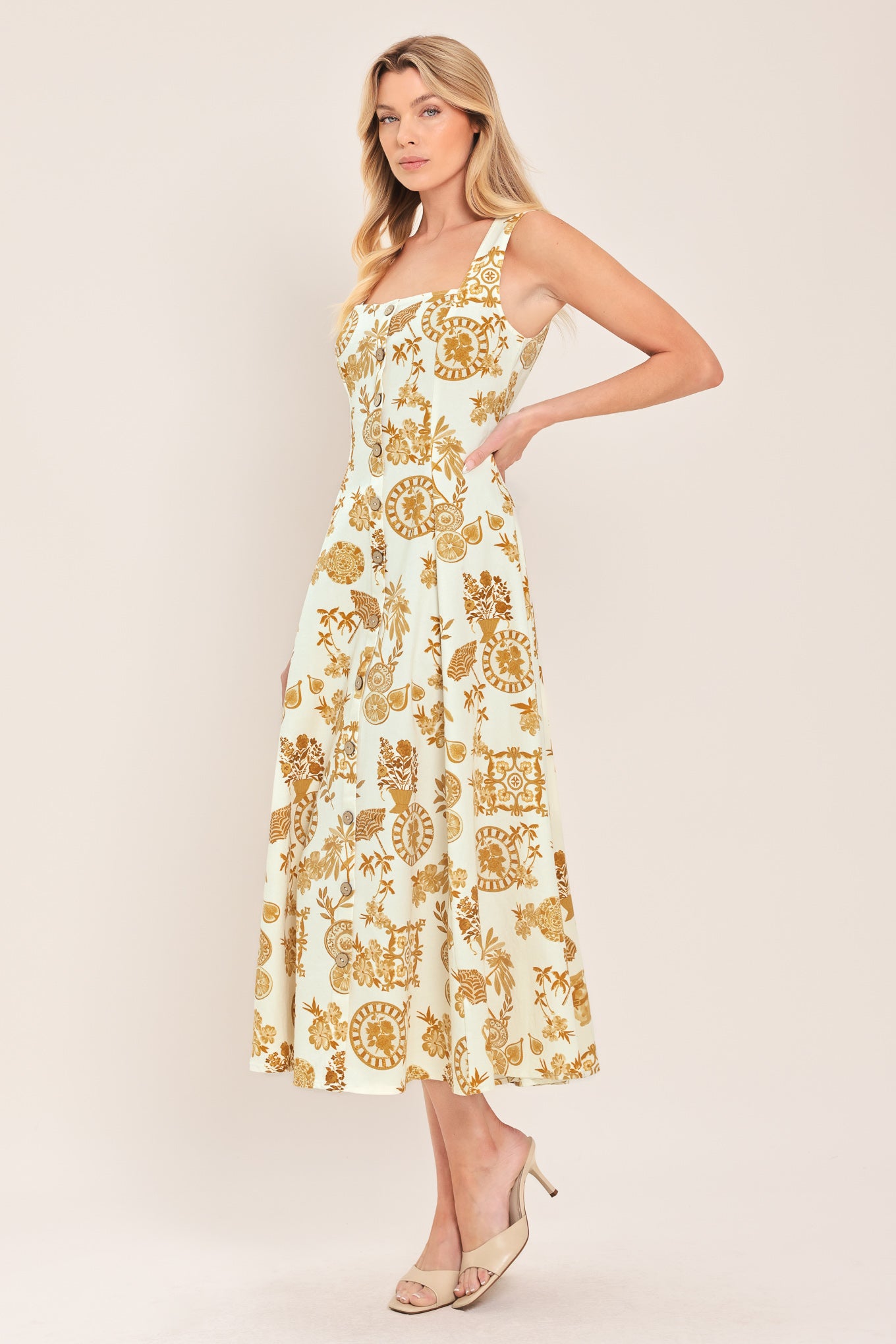 Woman wearing a yellow fruit and Mediterranean objects printed midi dress featuring square neckline, sleeveless, button down detail, circle skirt and back zipper closure | Flying Tomato