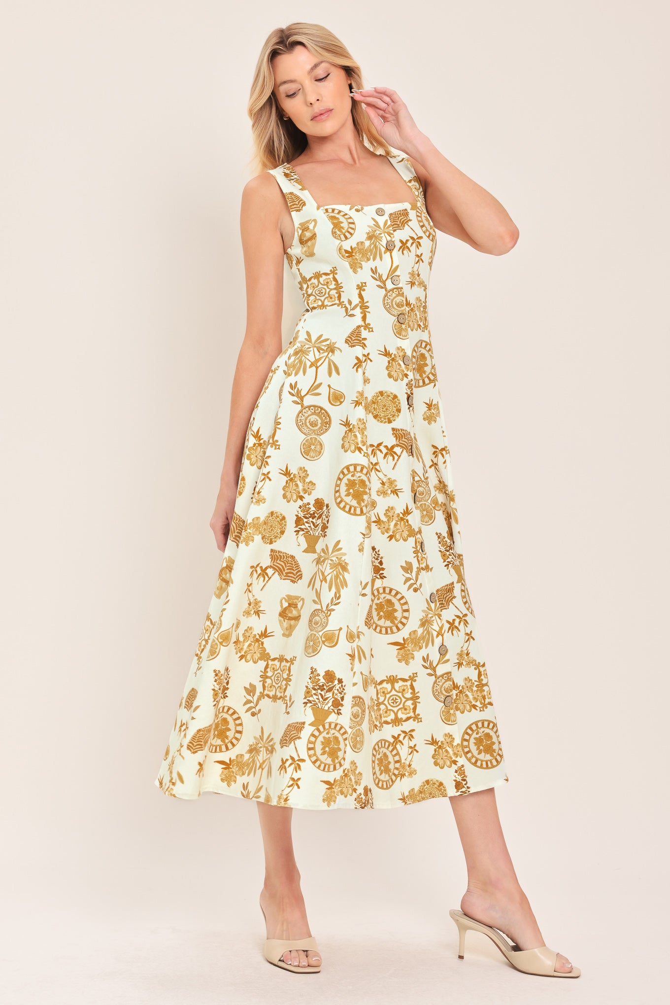 Woman wearing a yellow fruit and Mediterranean objects printed midi dress featuring square neckline, sleeveless, button down detail, circle skirt and back zipper closure | Flying Tomato