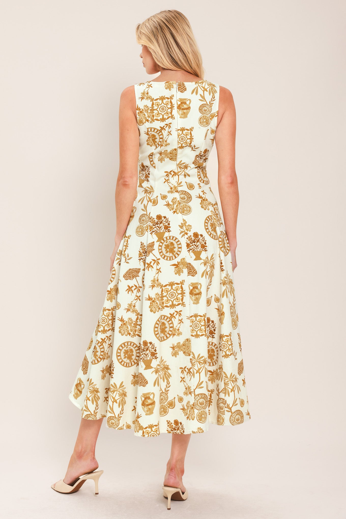 Woman wearing a yellow fruit and Mediterranean objects printed midi dress featuring square neckline, sleeveless, button down detail, circle skirt and back zipper closure | Flying Tomato