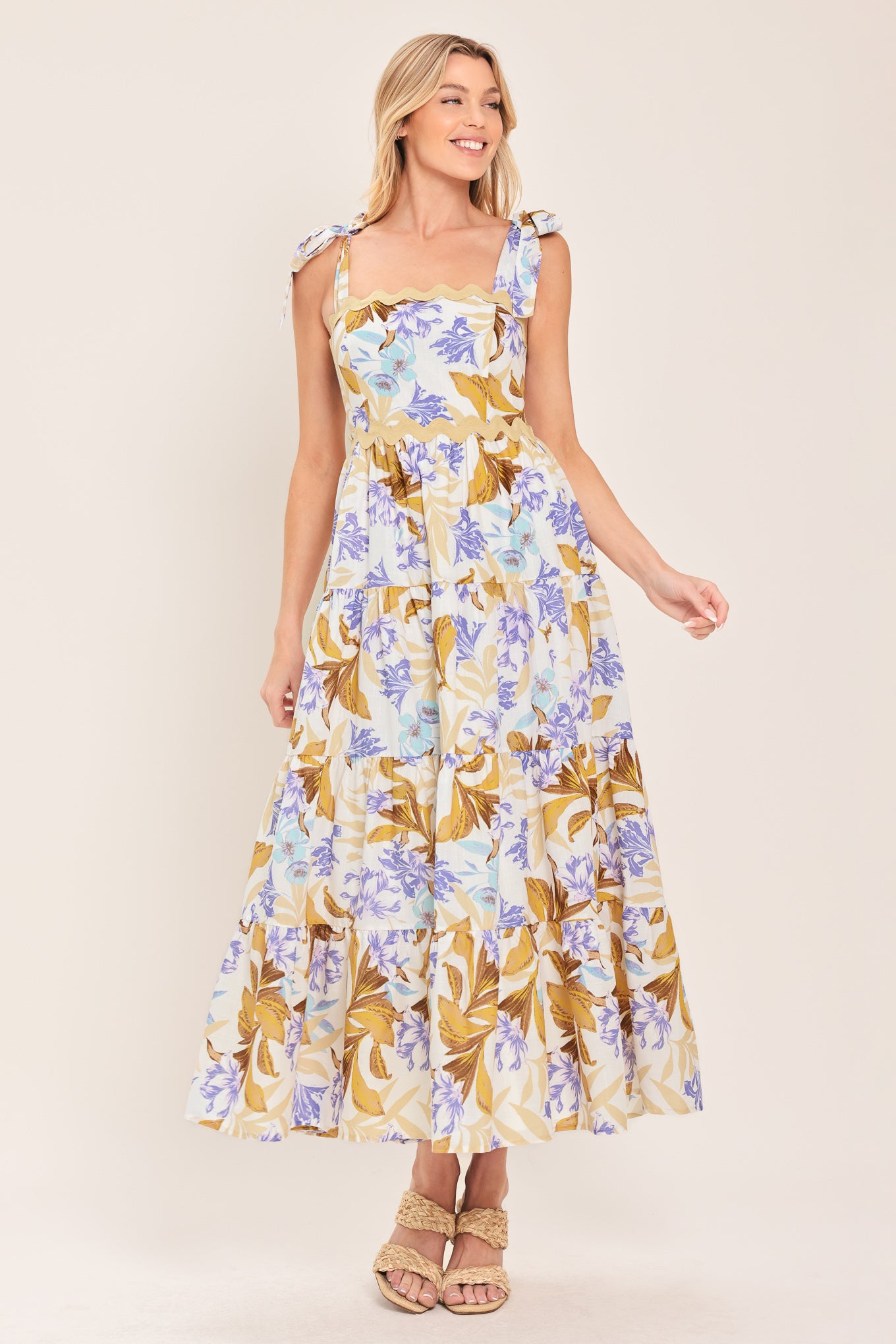 Woman wearing a floral midi dress featuring straight neckline with ric-rac trim, shoulder tie, tier skirt and smocked back bodice | Flying Tomato