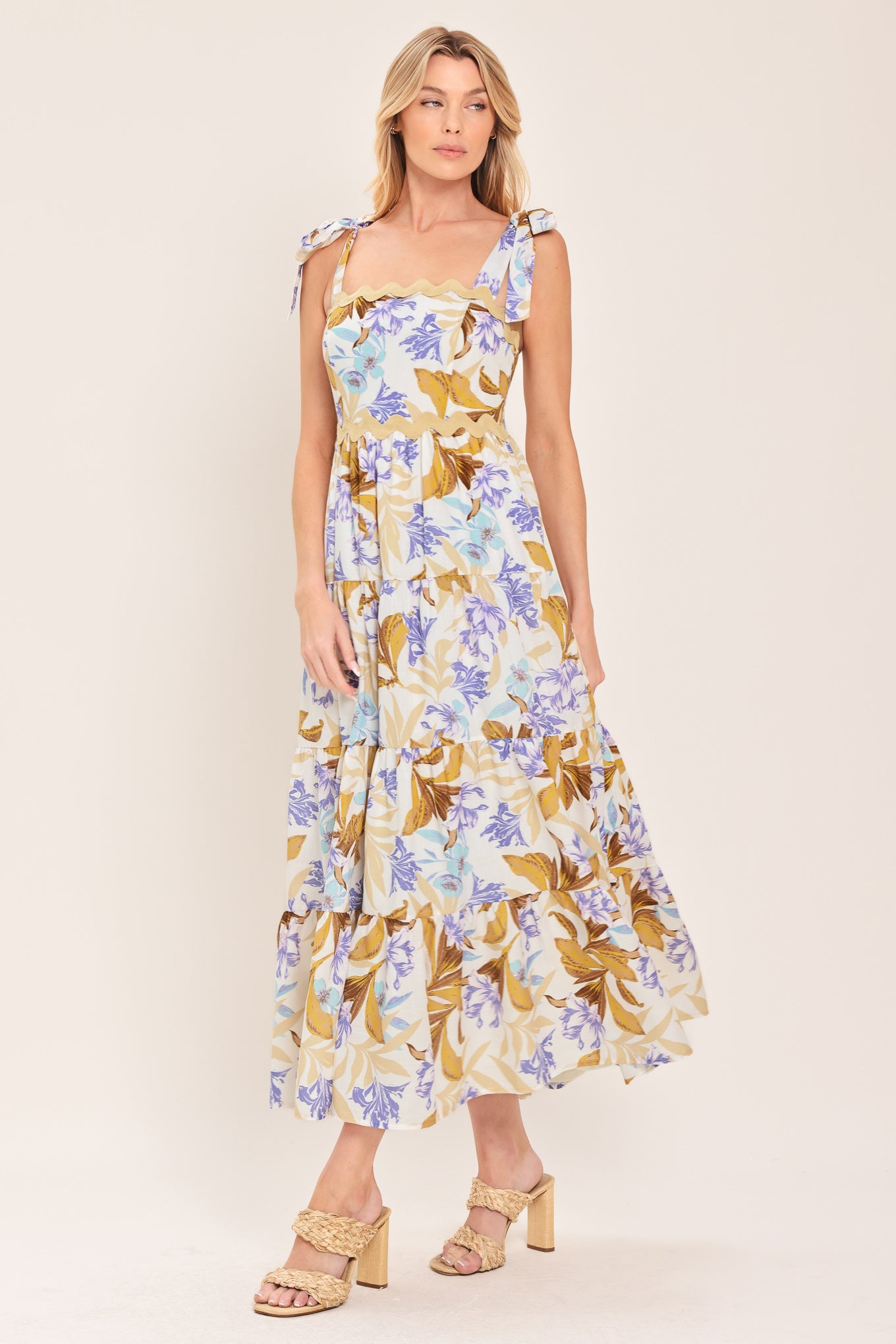 Woman wearing a floral midi dress featuring straight neckline with ric-rac trim, shoulder tie, tier skirt and smocked back bodice | Flying Tomato