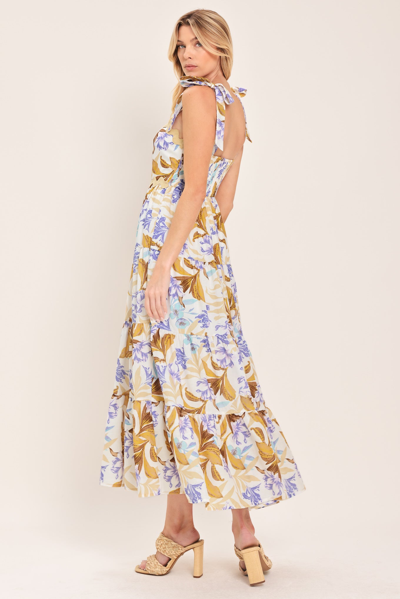 Woman wearing a floral midi dress featuring straight neckline with ric-rac trim, shoulder tie, tier skirt and smocked back bodice | Flying Tomato