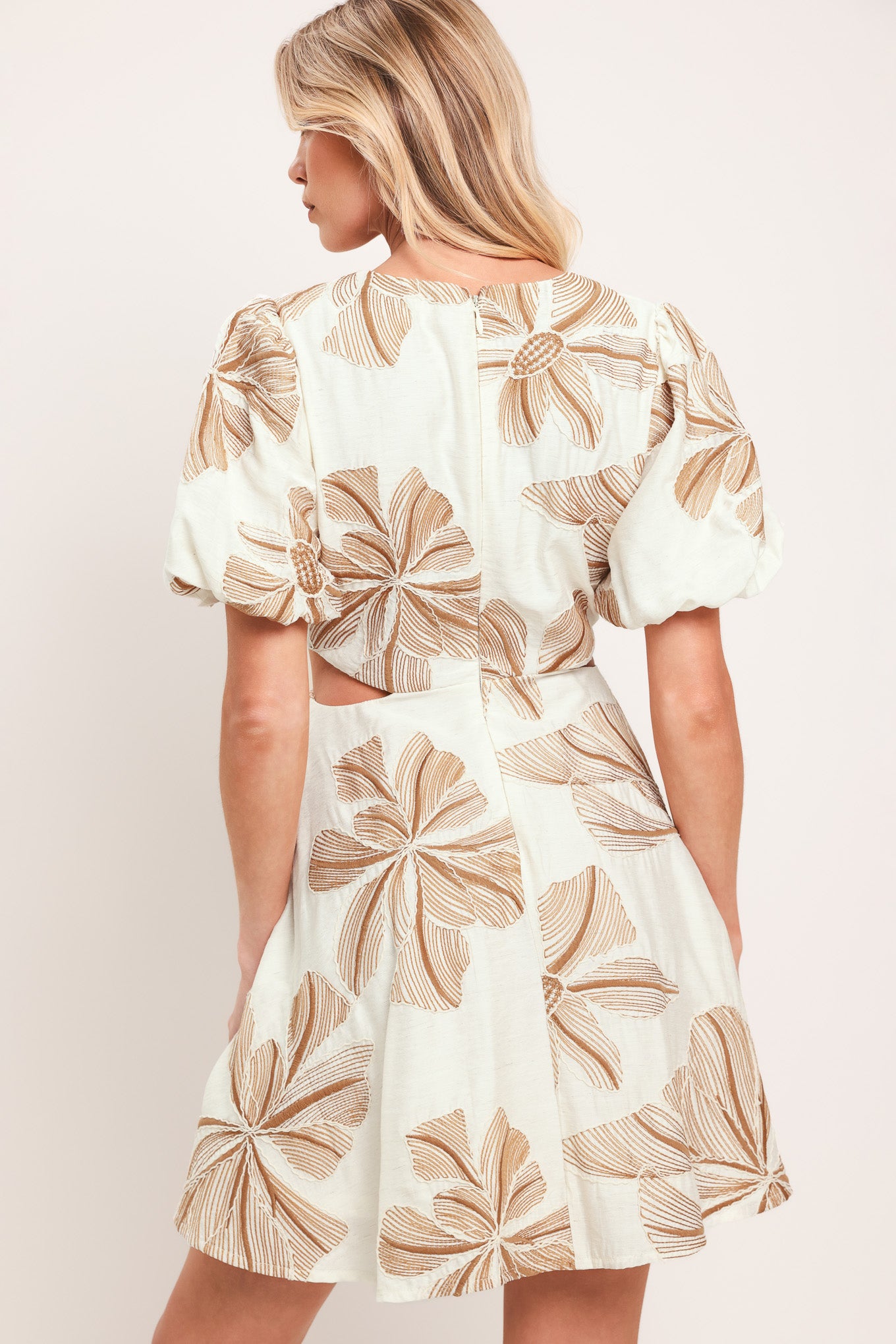 Woman wearing a white embroidered mini dress with brown leaf patterns and O ring gold belt, featuring V neckline, waist cut out, and back zipper closure | Flying Tomato