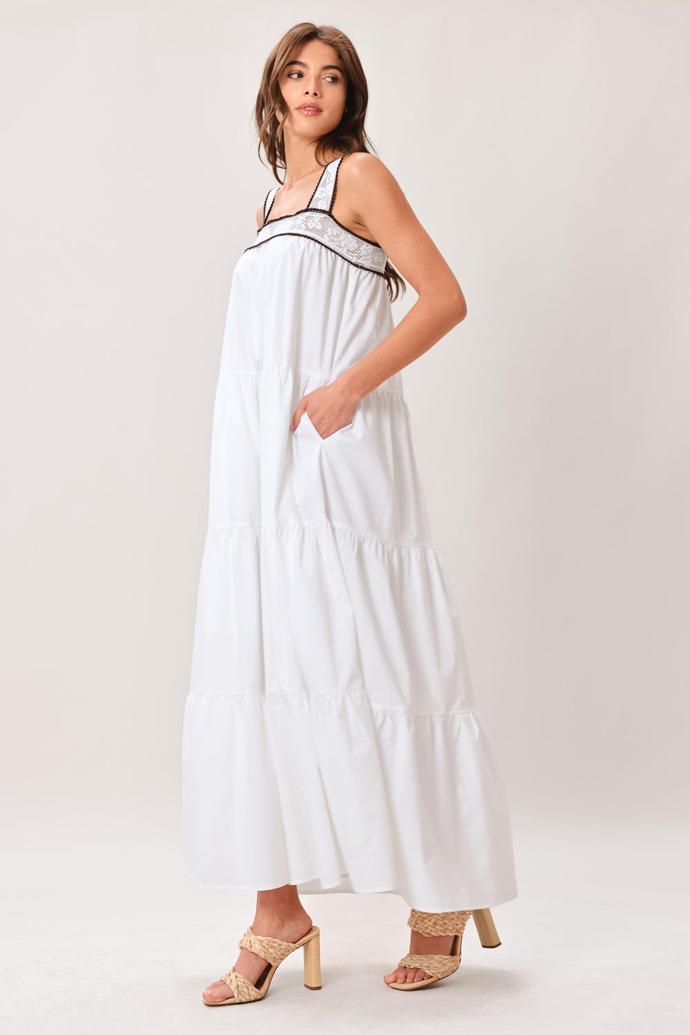 Woman wearing a white maxi dress featuring straight neckline with lace inset, wide lace inset strap, tier body and back zipper closure | Flying Tomato