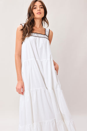 Woman wearing a white maxi dress featuring straight neckline with lace inset, wide lace inset strap, tier body and back zipper closure | Flying Tomato