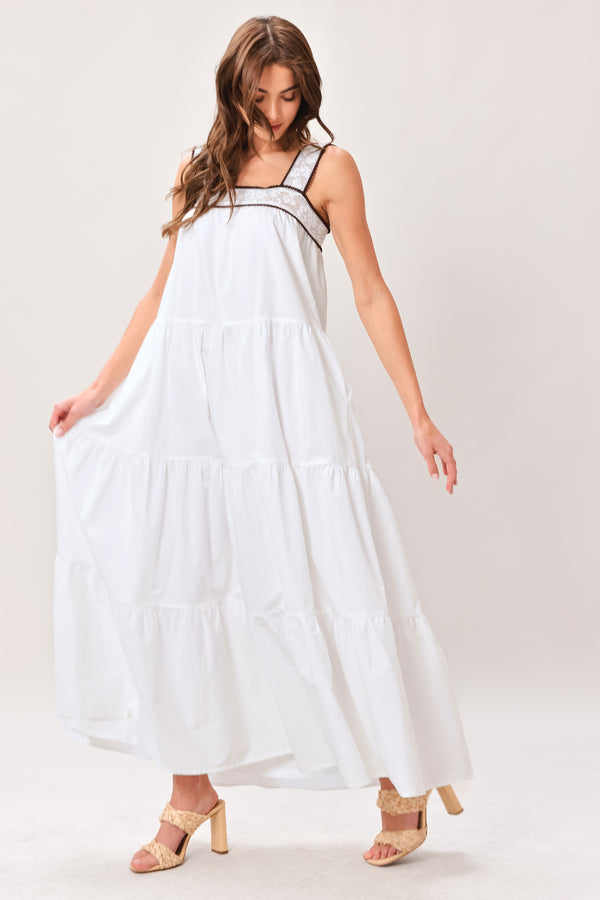 Woman wearing a white maxi dress featuring straight neckline with lace inset, wide lace inset strap, tier body and back zipper closure | Flying Tomato