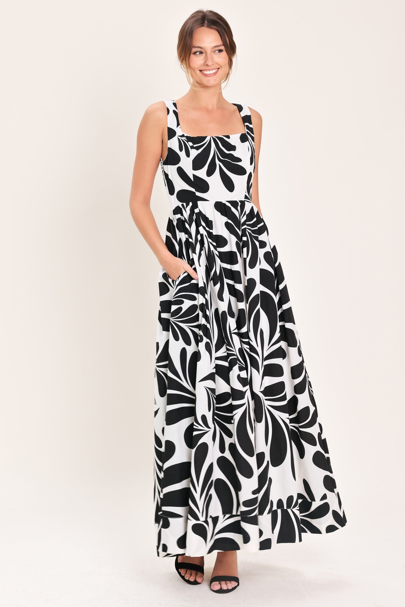 Woman wearing a black and white maxi dress featuring square neckline, sleeveless, full skirt, cut out back and button zipper closure | Flying Tomato