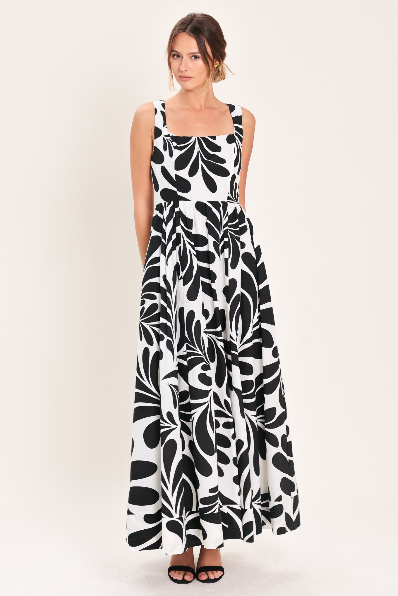Woman wearing a black and white maxi dress featuring square neckline, sleeveless, full skirt, cut out back and button zipper closure | Flying Tomato