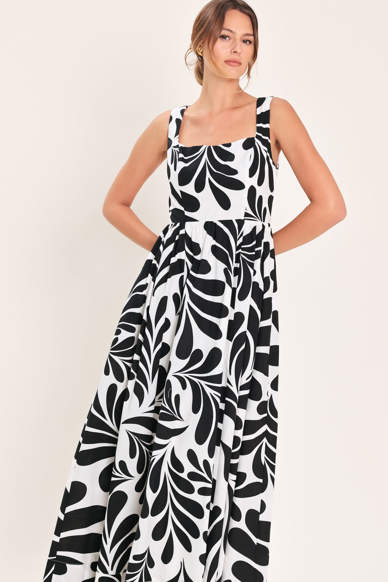 Woman wearing a black and white maxi dress featuring square neckline, sleeveless, full skirt, cut out back and button zipper closure | Flying Tomato
