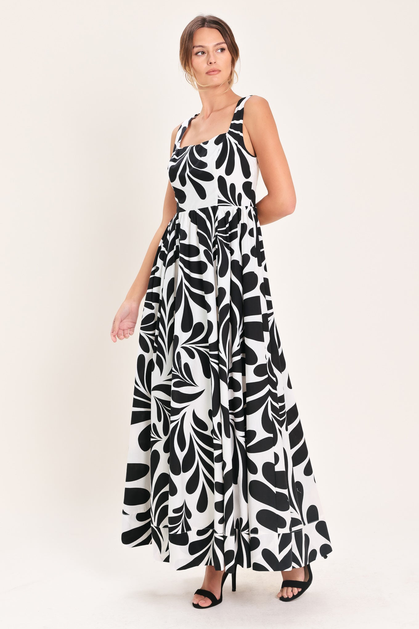 Woman wearing a black and white maxi dress featuring square neckline, sleeveless, full skirt, cut out back and button zipper closure | Flying Tomato