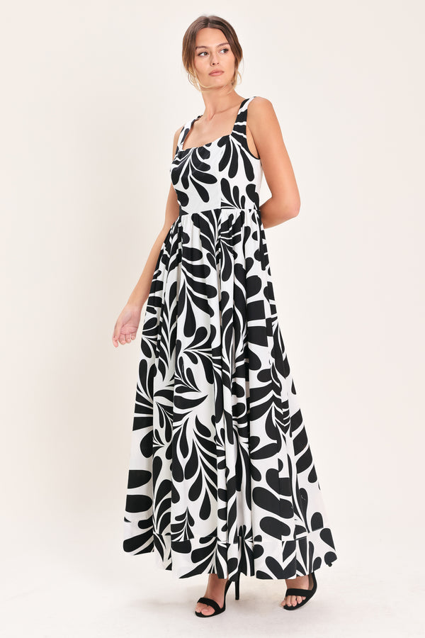 Woman wearing a black and white maxi dress featuring square neckline, sleeveless, full skirt, cut out back and button zipper closure | Flying Tomato