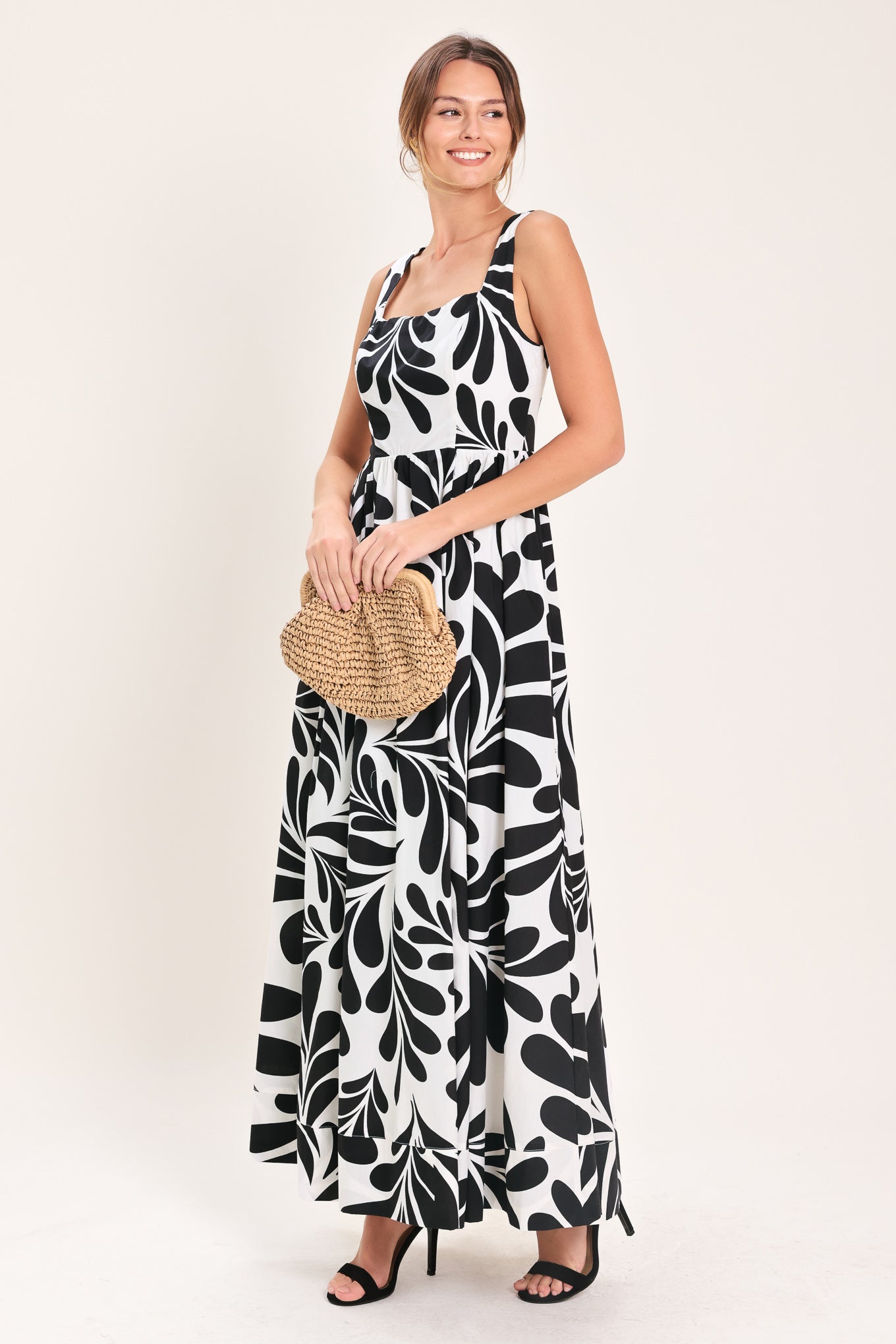 Woman wearing a black and white maxi dress featuring square neckline, sleeveless, full skirt, cut out back and button zipper closure | Flying Tomato