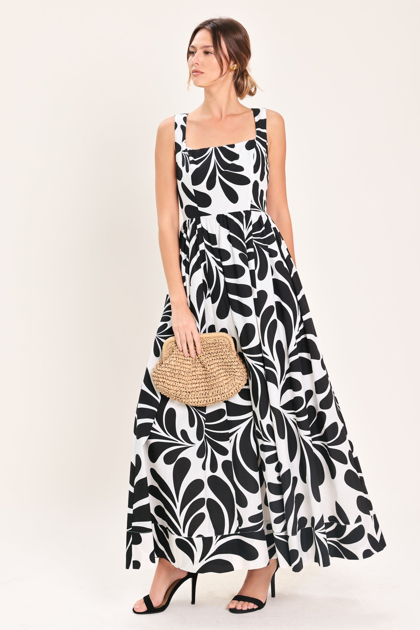 Woman wearing a black and white maxi dress featuring square neckline, sleeveless, full skirt, cut out back and button zipper closure | Flying Tomato