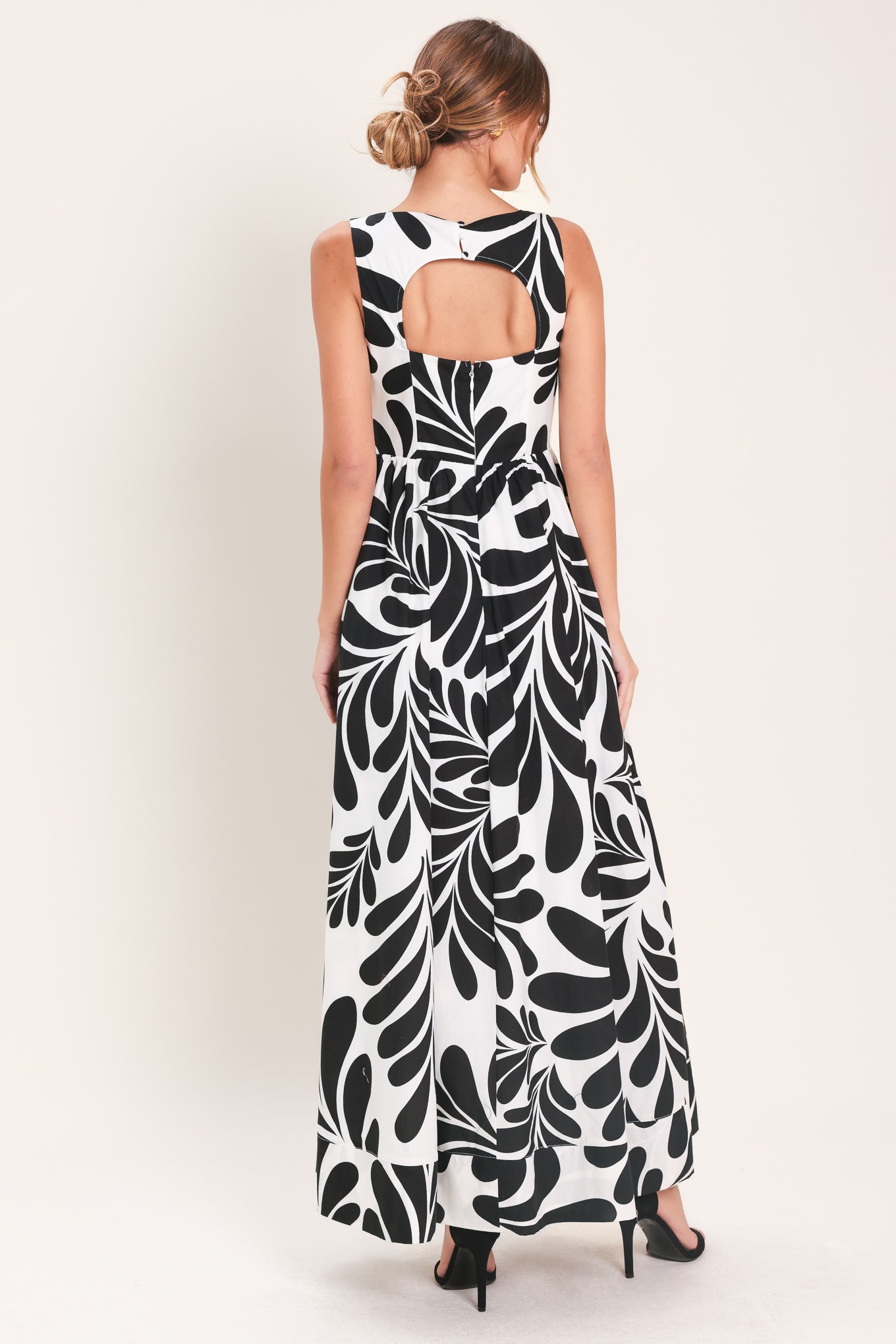 Woman wearing a black and white maxi dress featuring square neckline, sleeveless, full skirt, cut out back and button zipper closure | Flying Tomato