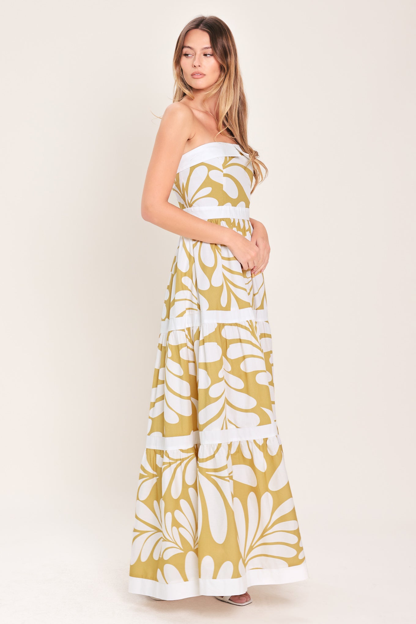 Woman wearing a beige and white  maxi dress featuring strapless neckline, tier skirt and back zipper closure | Flying Tomato