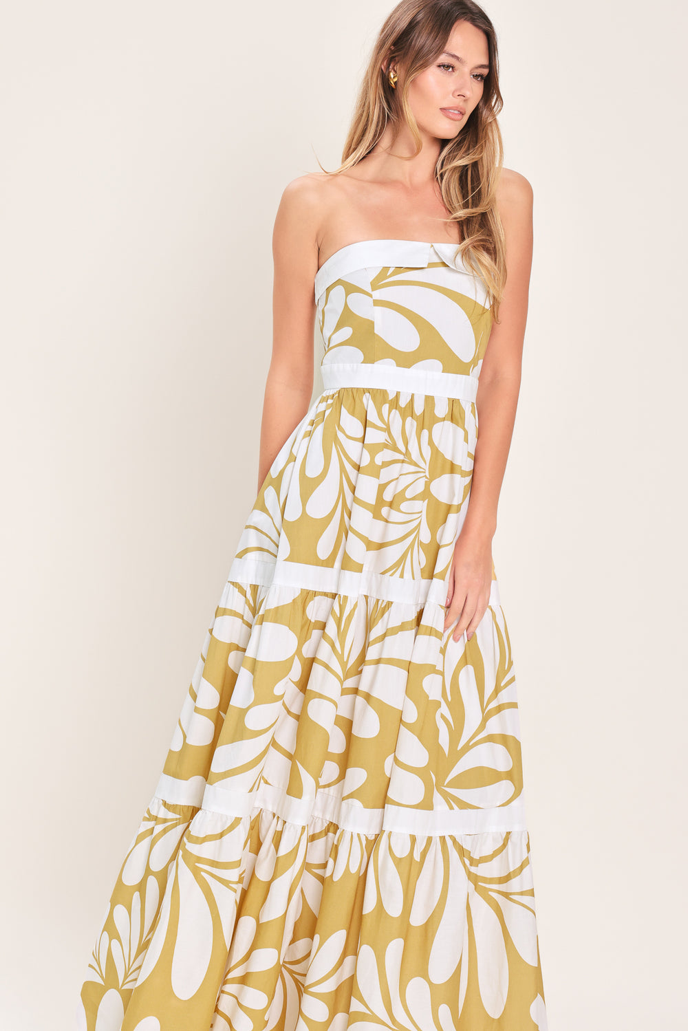 Woman wearing a beige and white  maxi dress featuring strapless neckline, tier skirt and back zipper closure | Flying Tomato